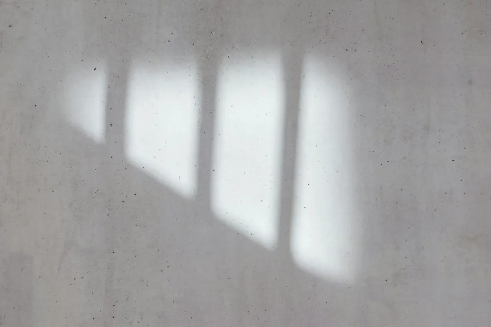 Soft daylight from a window falling across a bare concrete wall.