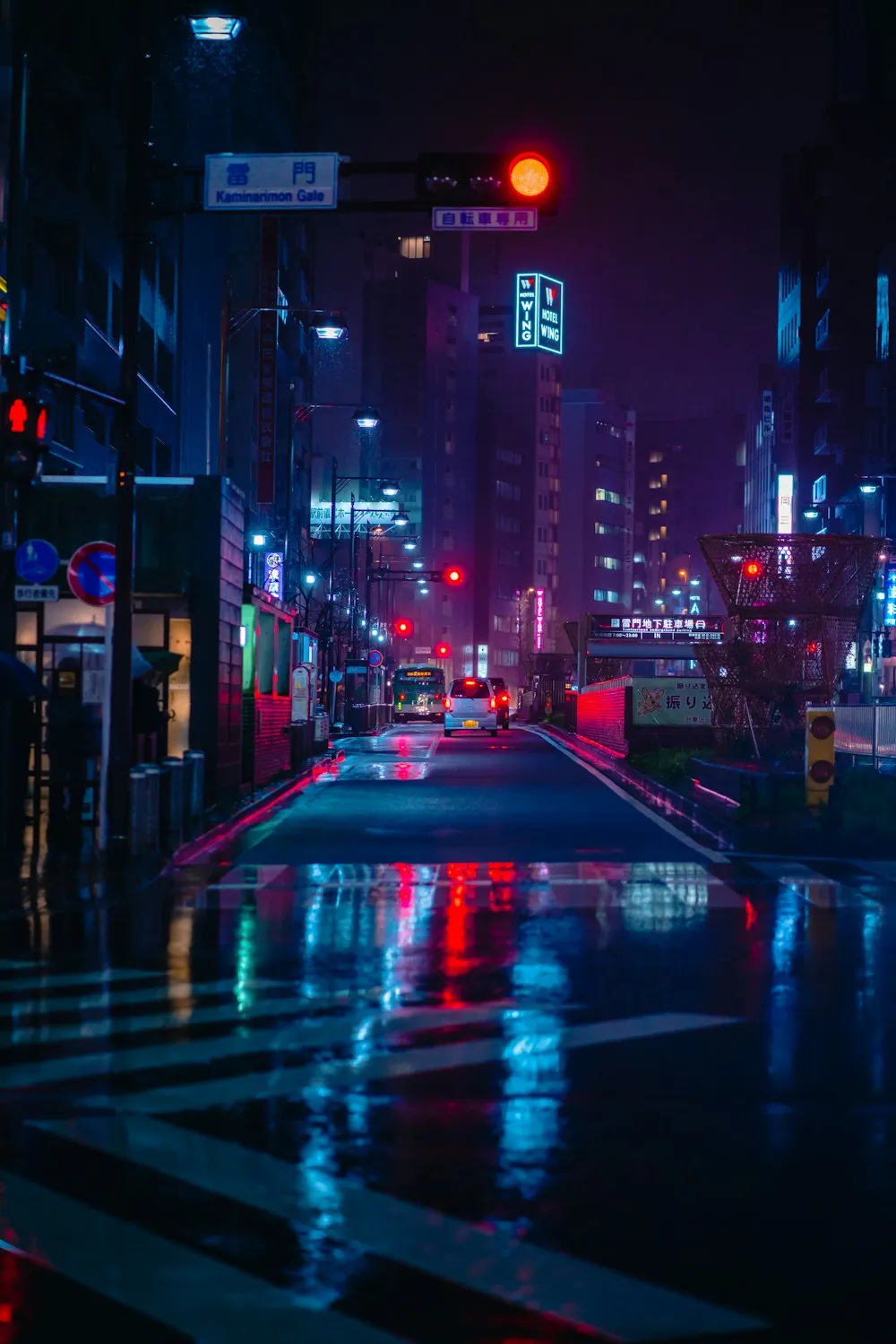 A wet city street at night, lit by neon signs.