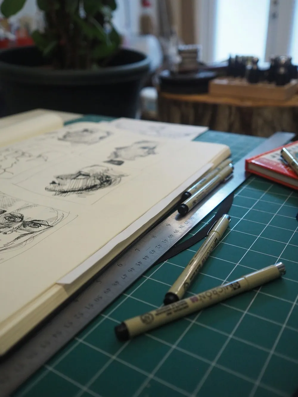 An open sketchbook with ink drawings beside pens and a ruler.